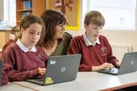 Rowandale Primary School teacher assisting two primary school students working on laptops at a classroom table.