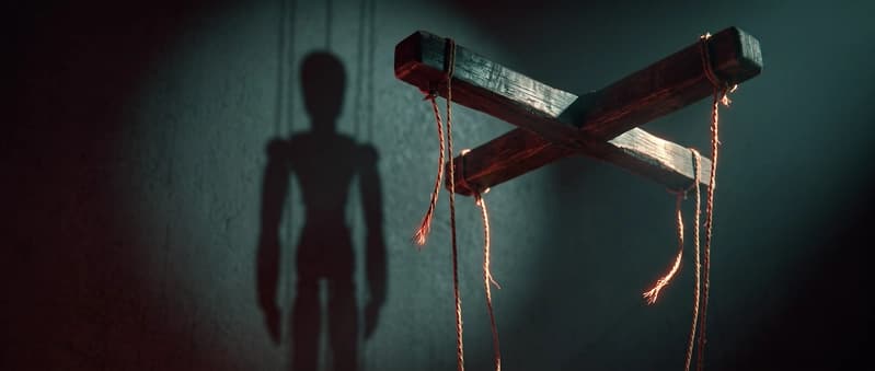 A puppet's control bar with its strings severed, the puppet's shadow still standing on the wall behind it